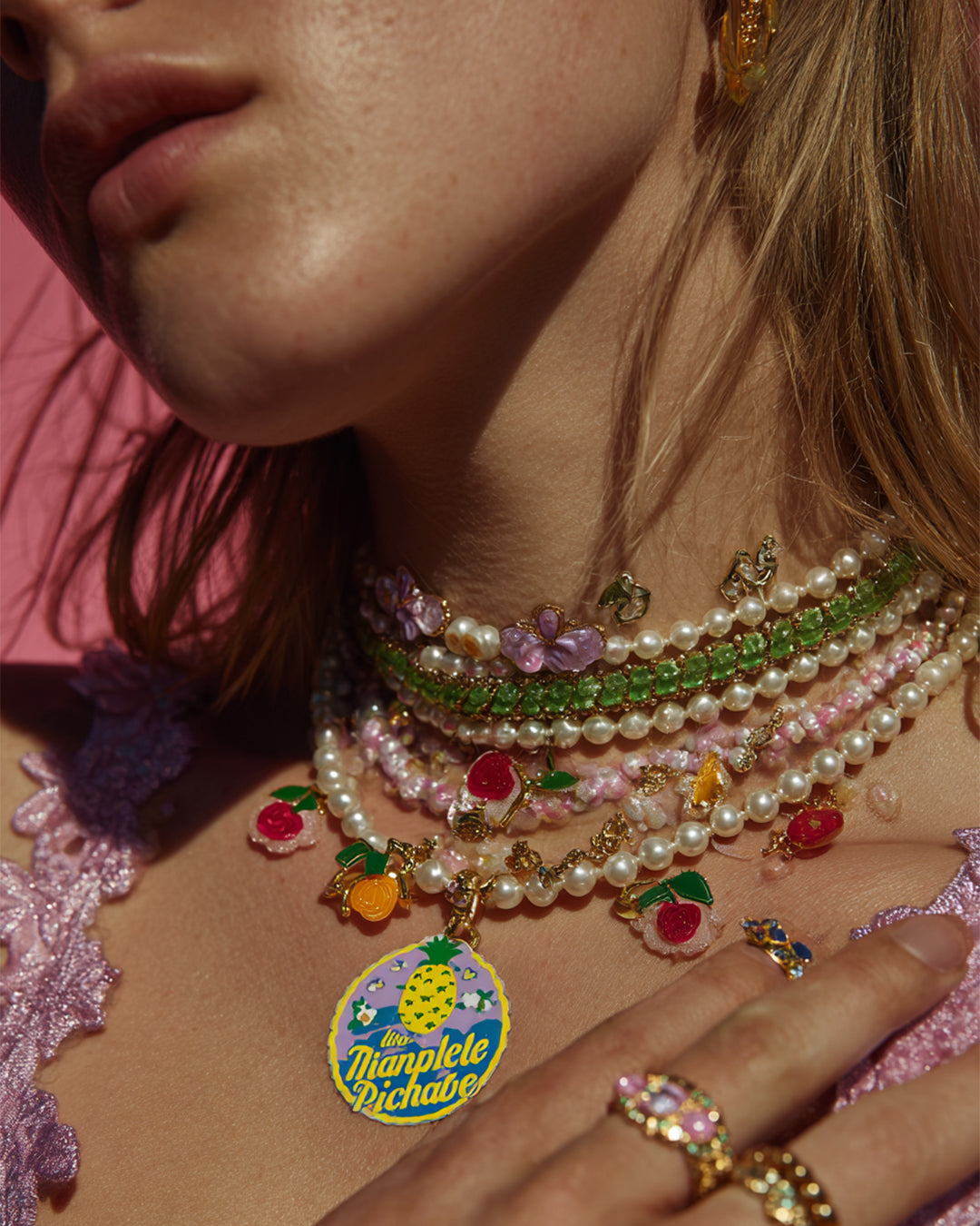 Woman wearing layered pearl and beaded necklaces with fruit charms and colorful rings on hand, styled in a vibrant summer jewelry look.