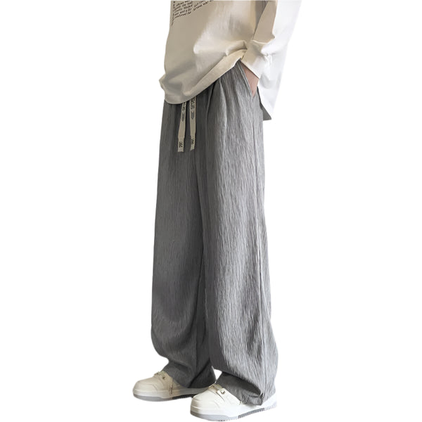 Person wearing gray wide-leg pants and a white shirt against a plain wall.